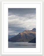 Moody storm clouds, sun-lit peak over Lakeside peaks in Queenstown New Zealand