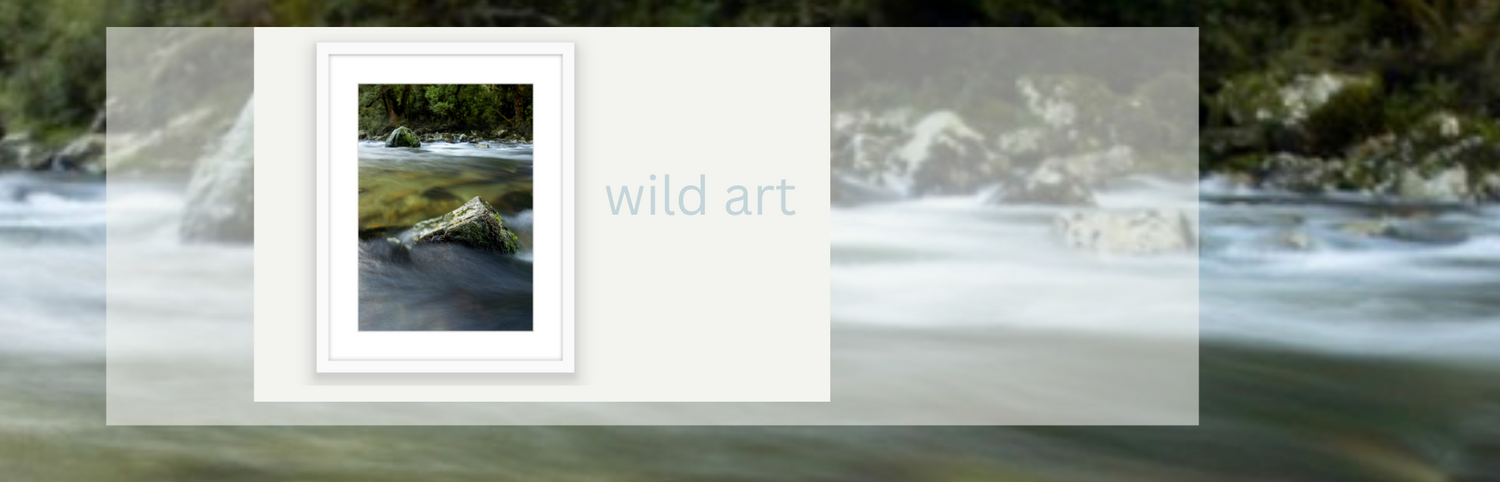 Framed Blankwallnz art photography featuring a river flowing over rocks, shown as a mockup overlay on a blurred background of a rocky river.