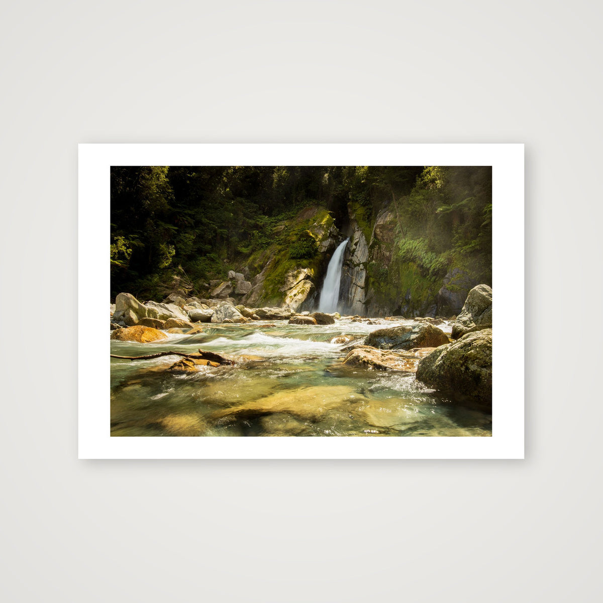 A magnificent long exposure of the pounding waters of Giant Gate Falls in Fiordland World Heritage park, Aotearoa New Zealand. The rich honey river rocks impact a golden sheen to the crystal clear green sage waters.