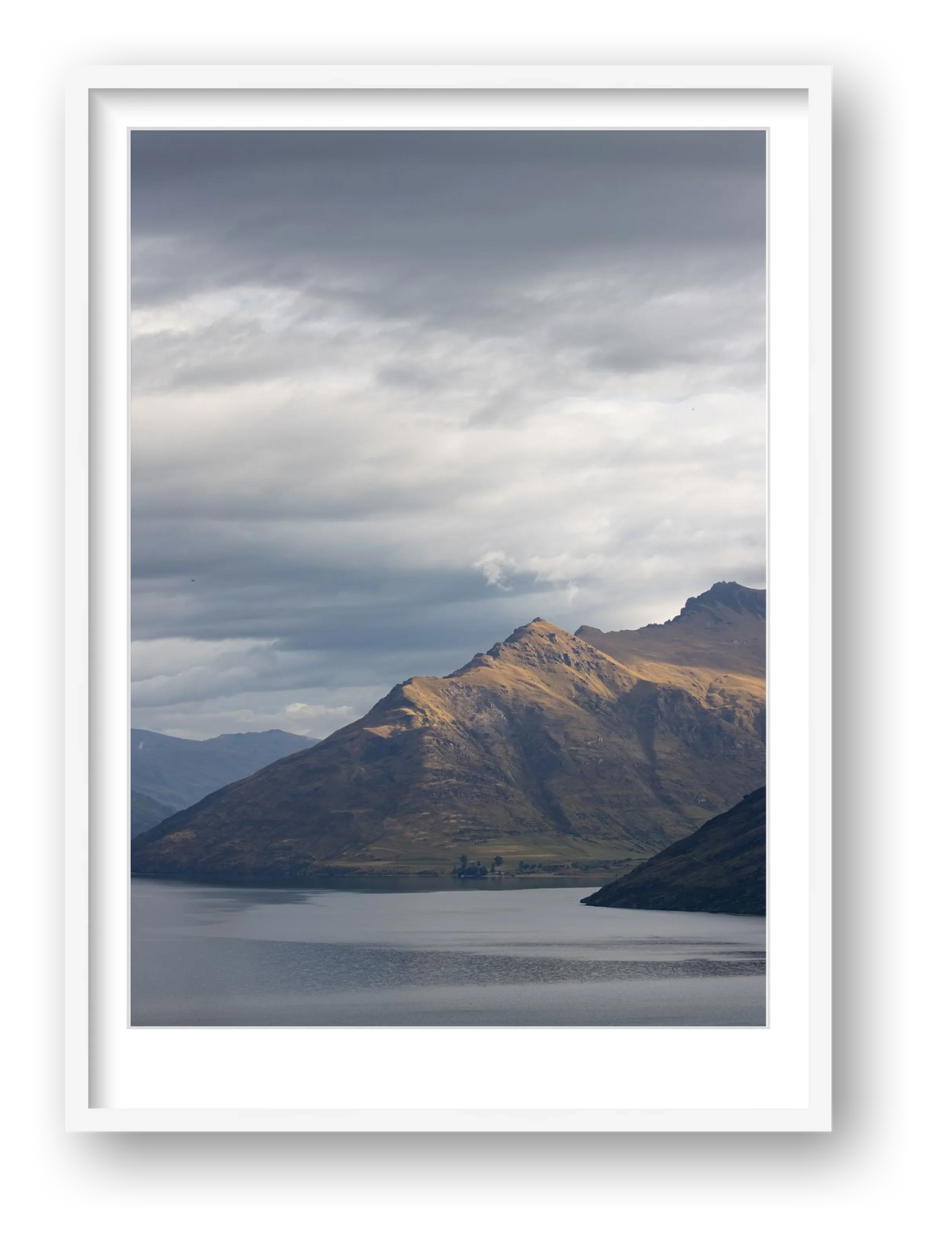 Moody storm clouds, sun-lit peak over Lakeside peaks in Queenstown New Zealand. An bright white frame that encircles the russett from native tussock and moody deep grey blues. 