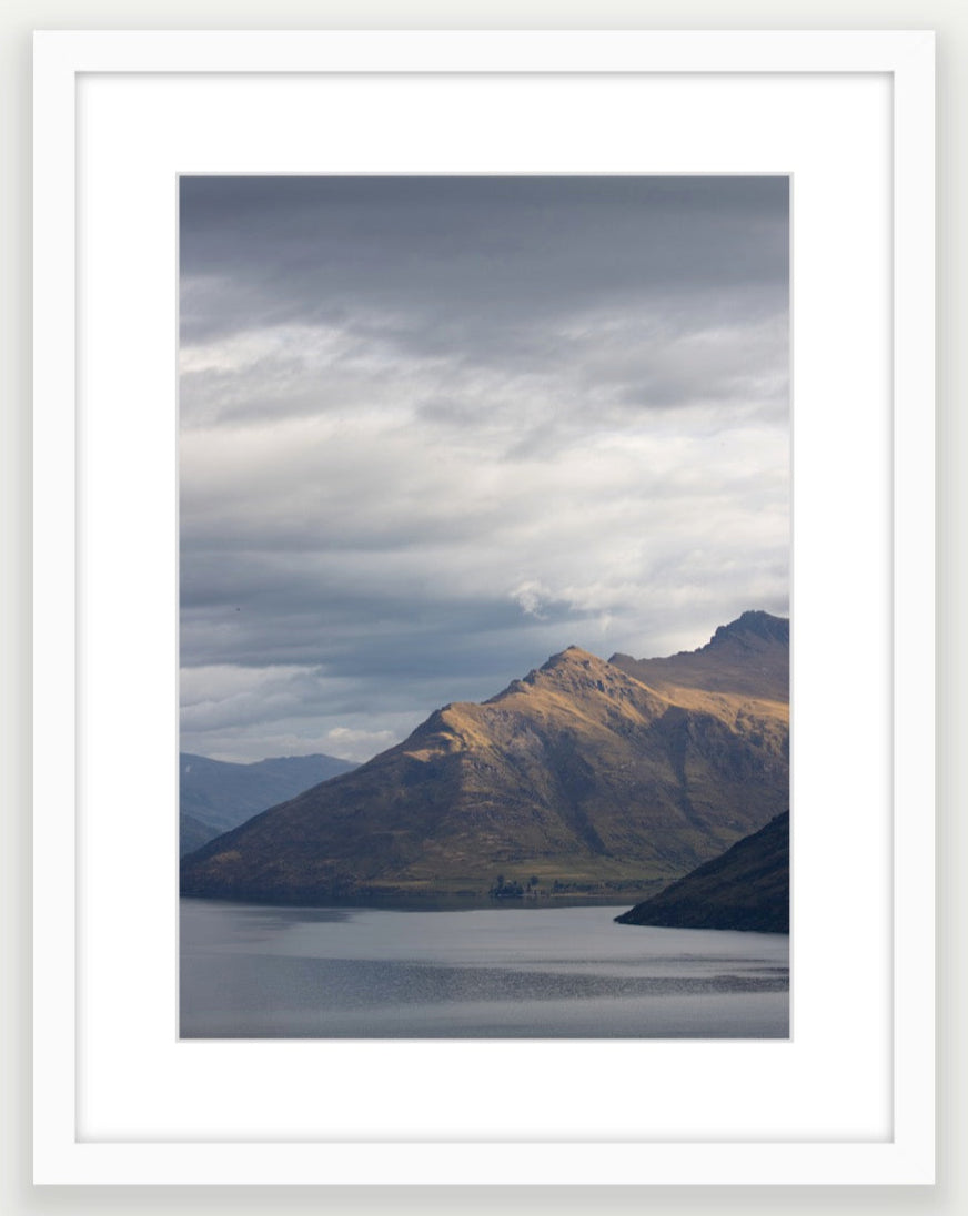 Moody storm clouds, sun-lit peak over Lakeside peaks in Queenstown New Zealand. Premium White Wood A3 Framed art.