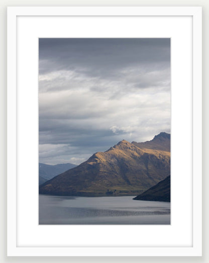 Moody storm clouds, sun-lit peak over Lakeside peaks in Queenstown New Zealand. Premium White Wood A3 Framed art.