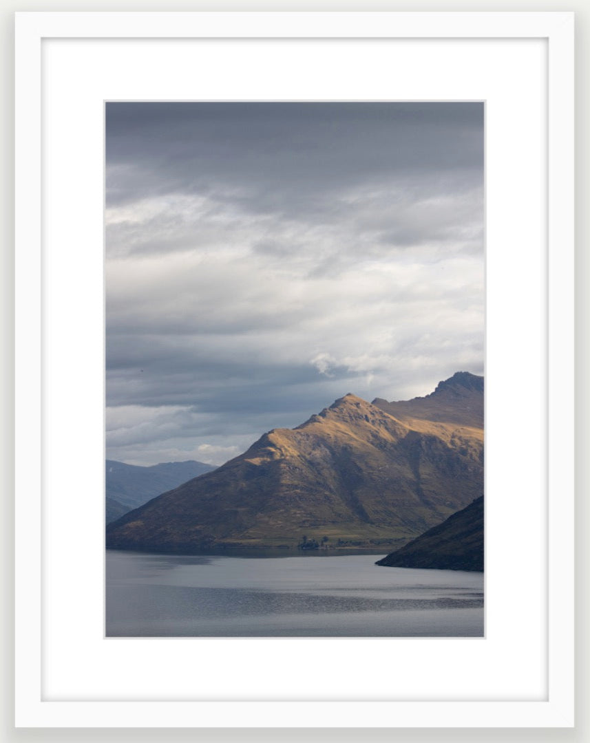 Moody storm clouds, sun-lit peak over Lakeside peaks in Queenstown New Zealand. Memories of New Zealand.