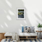 A framed waterscape river art photography of a river and forest hangs on a white wall above a modern lounge setting. 