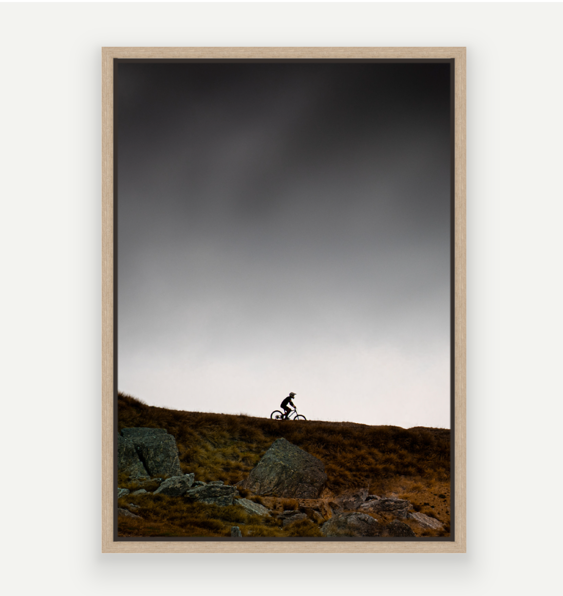 Framed artwork of a mountain biker on a hillside with a dark sky.