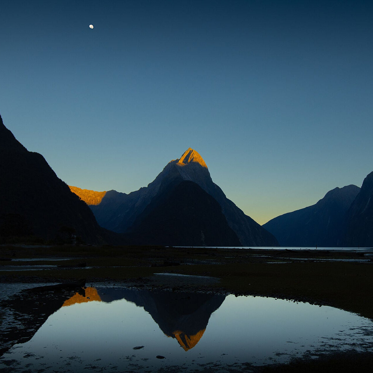 Mitre Peak at dawn, showing her red tips of dawn known as te atakura in te rea Māori. All reflected in the still dawn sea of Milford Sound